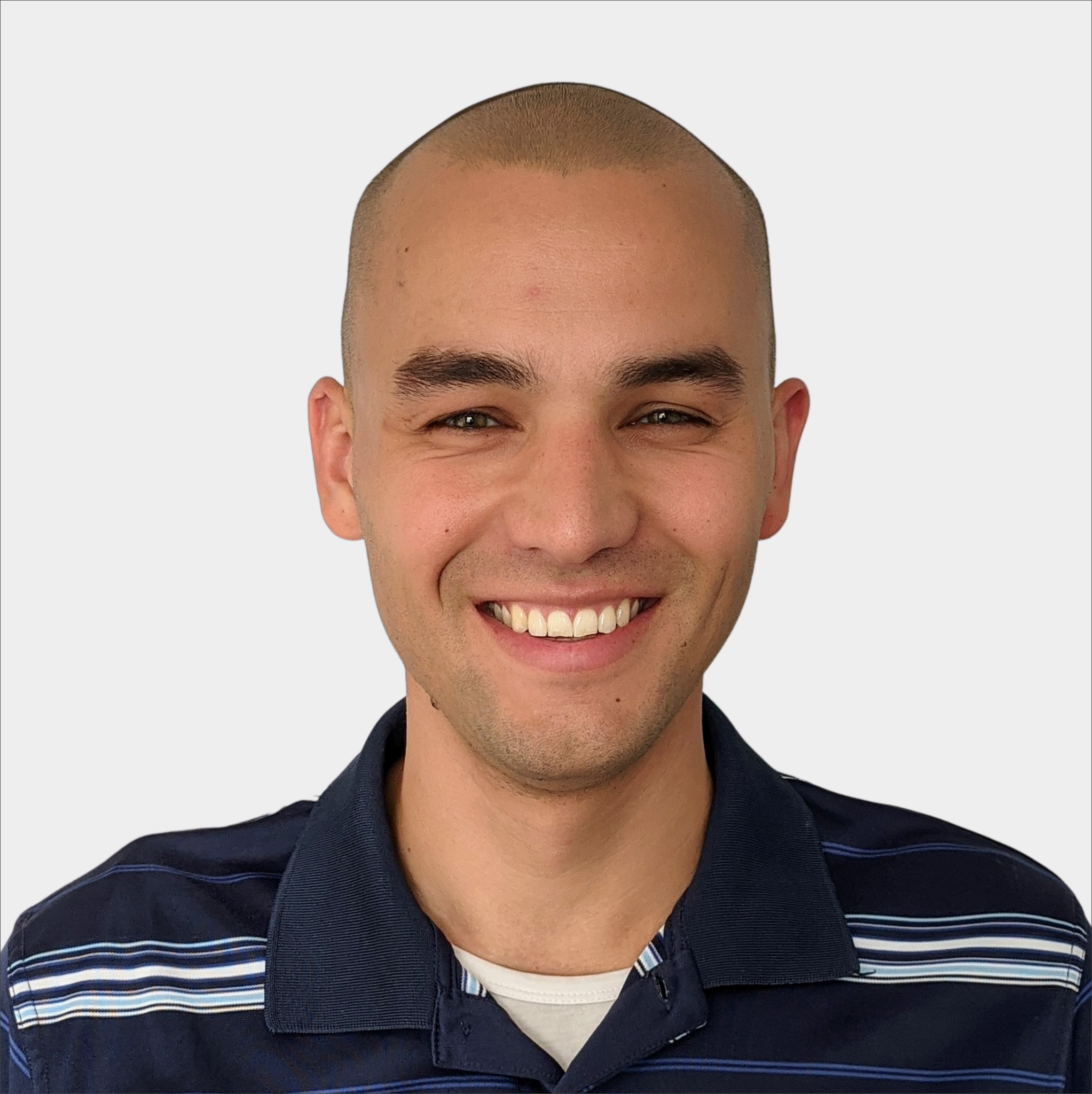 A person with a shaved head and dark eyebrows smiles while wearing a navy blue collared shirt with white stripes, in front of a plain light background.